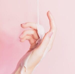 A Hand on Pink Background With Lotion Falling
