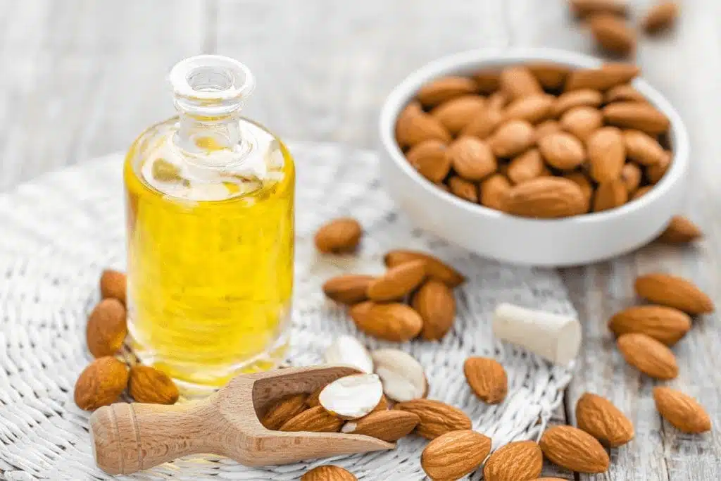 Bottle of almond oil surrounded by raw almonds