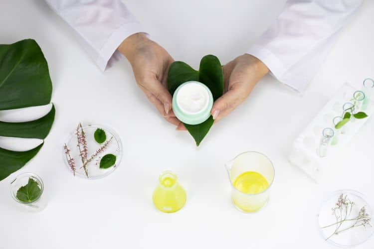 woman holding jar of cream and heart-shaped leaf, surrounded by lab equipment