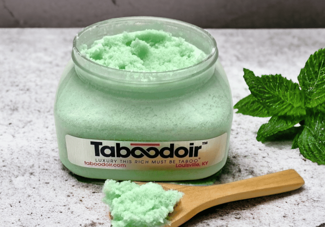 Open jar of Taboodoir Mint to Tease Body Polish with a wooden spoon and fresh mint leaves