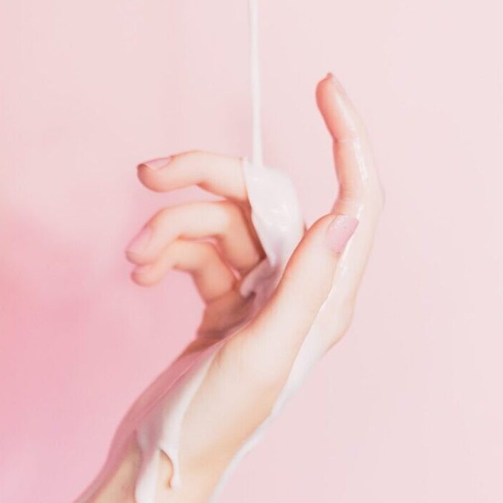 A Hand on Pink Background With Lotion Falling